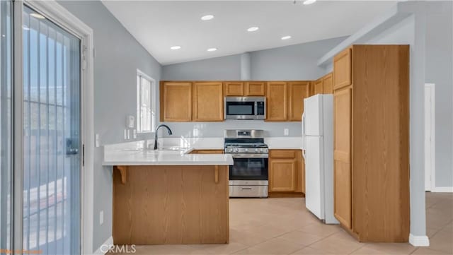 kitchen featuring stainless steel appliances, a peninsula, a sink, vaulted ceiling, and light countertops