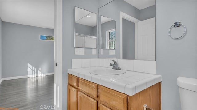 bathroom featuring toilet, wood finished floors, vanity, a healthy amount of sunlight, and baseboards