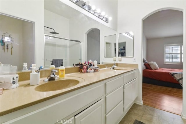 ensuite bathroom featuring a stall shower, tile patterned flooring, a sink, and double vanity