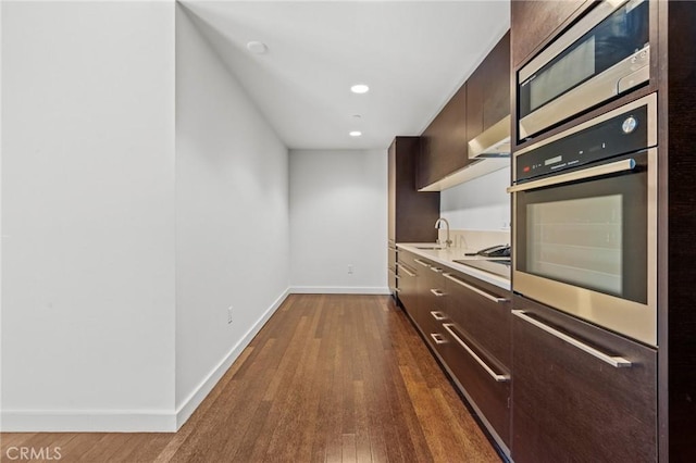 kitchen featuring dark wood-type flooring, dark brown cabinets, appliances with stainless steel finishes, light countertops, and modern cabinets