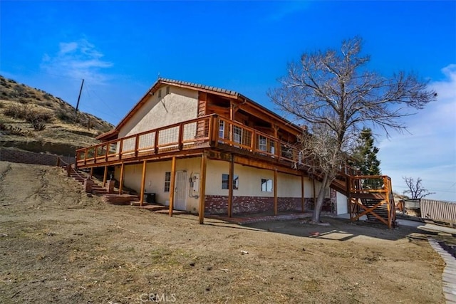 rear view of house with stairs, a wooden deck, and stucco siding