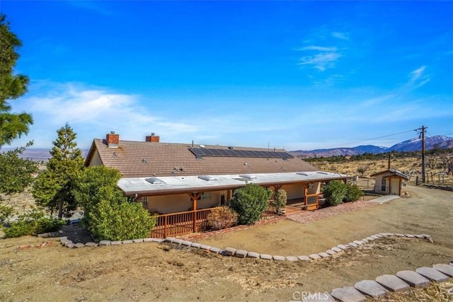 back of property featuring covered porch, a mountain view, a chimney, and solar panels