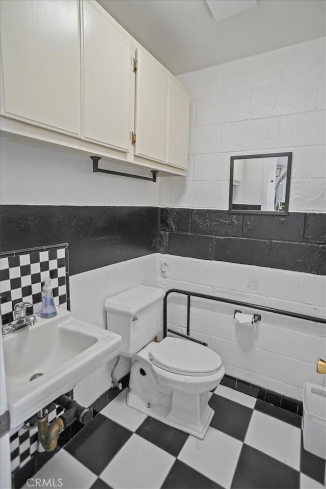 half bath with tile walls, tasteful backsplash, toilet, a sink, and tile patterned floors