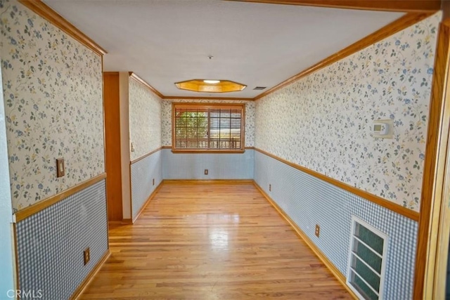 empty room with wallpapered walls, light wood finished floors, crown molding, and wainscoting