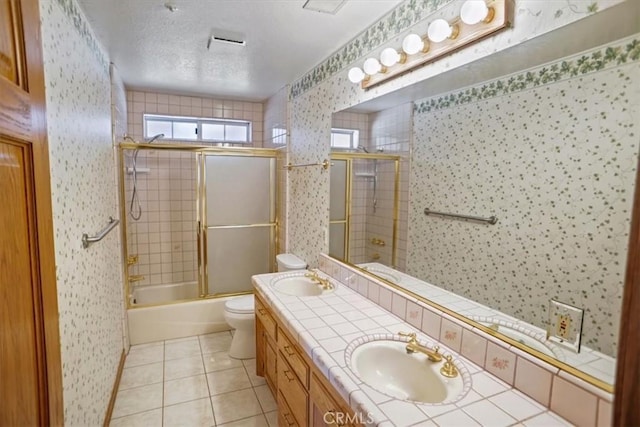 bathroom with a textured ceiling, tile patterned flooring, toilet, a sink, and wallpapered walls