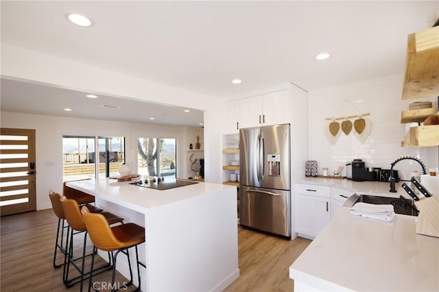 kitchen with black electric stovetop, stainless steel fridge with ice dispenser, light wood-style flooring, a kitchen island, and a kitchen bar