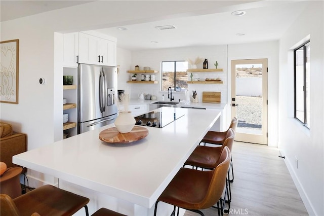 kitchen featuring stainless steel fridge with ice dispenser, black electric stovetop, a kitchen bar, open shelves, and a sink