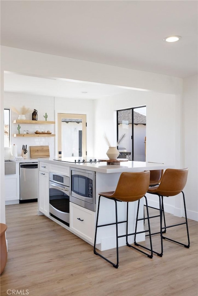 kitchen with a breakfast bar area, open shelves, stainless steel appliances, light wood-style floors, and white cabinets