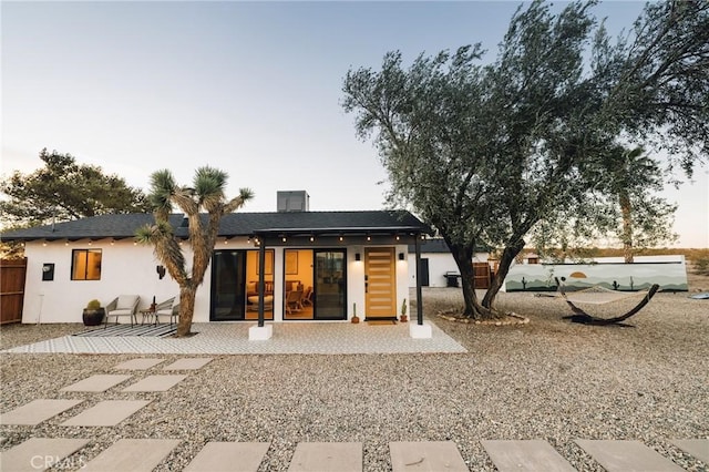 rear view of house with a patio, fence, and stucco siding