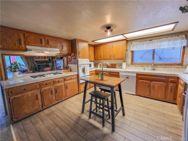 kitchen featuring white appliances, light wood-type flooring, brown cabinets, and under cabinet range hood