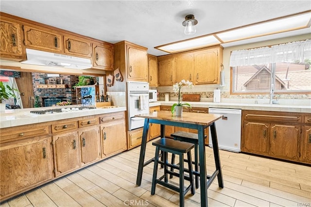 kitchen with white appliances, brown cabinets, light wood-style flooring, and under cabinet range hood