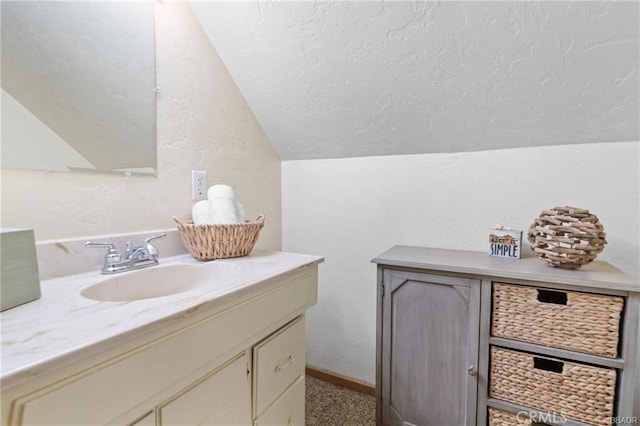 bathroom with a textured ceiling, a textured wall, lofted ceiling, vanity, and baseboards