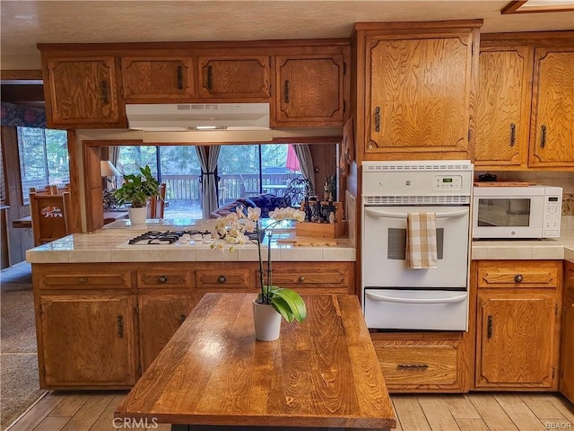 kitchen featuring a warming drawer, white microwave, brown cabinetry, and exhaust hood