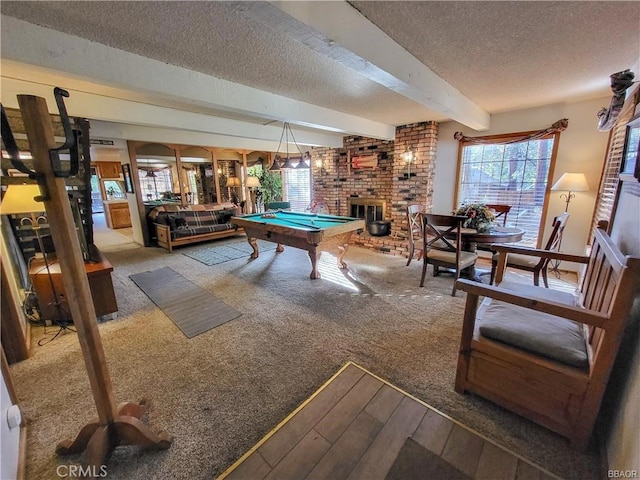 rec room featuring a textured ceiling, pool table, carpet flooring, a brick fireplace, and beamed ceiling