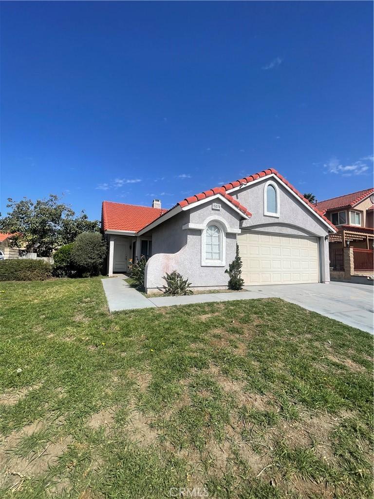 view of front of home with stucco siding, driveway, a front lawn, an attached garage, and a tiled roof