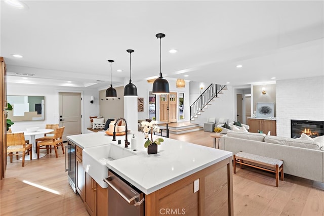 kitchen featuring light wood-style flooring, recessed lighting, a fireplace, a sink, and dishwasher