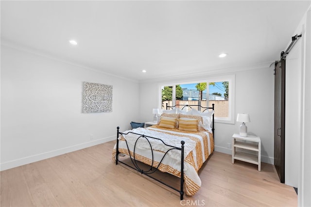 bedroom with ornamental molding, baseboards, light wood finished floors, and a barn door