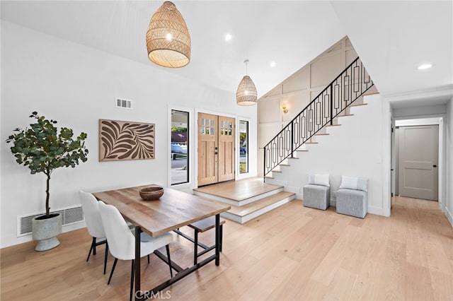 dining space with light wood-type flooring, high vaulted ceiling, stairs, and visible vents