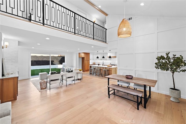 dining room with visible vents, light wood finished floors, a high ceiling, and a decorative wall