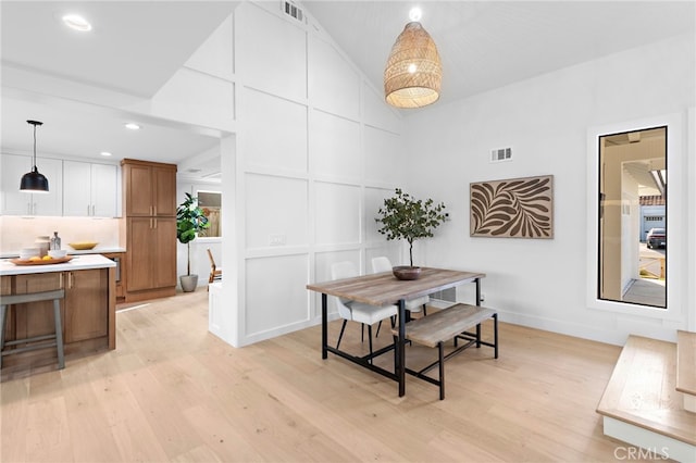 dining area featuring lofted ceiling, visible vents, a decorative wall, and light wood finished floors