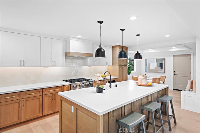 kitchen featuring a breakfast bar, an island with sink, stainless steel range with gas stovetop, and light wood-style floors