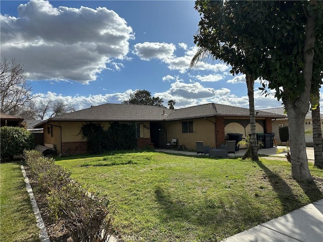 view of front of property featuring a patio, brick siding, a front yard, and stucco siding