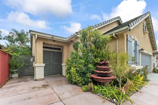 view of front of home with stucco siding, driveway, a garage, and fence