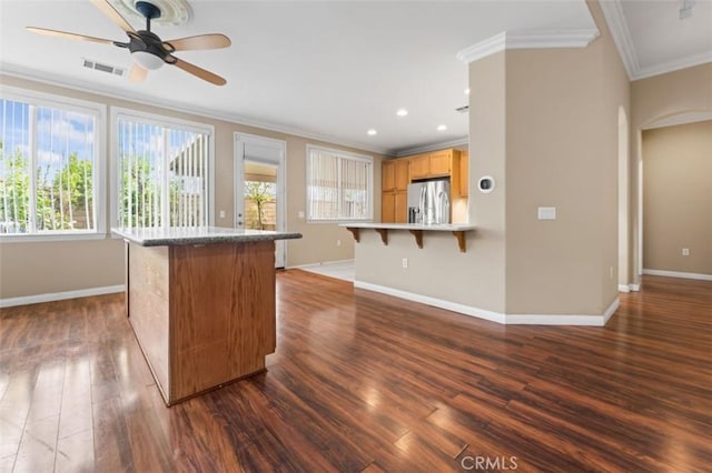 kitchen featuring visible vents, ceiling fan, stainless steel refrigerator with ice dispenser, a kitchen bar, and crown molding