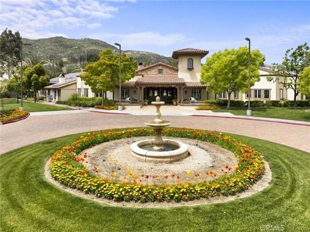 view of property's community featuring a lawn, a mountain view, and curved driveway