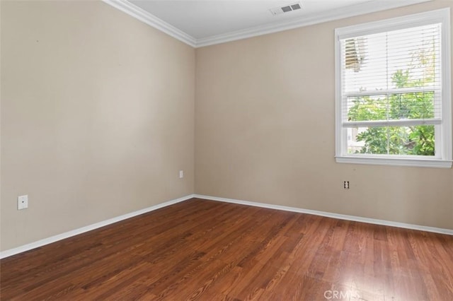 empty room with visible vents, wood finished floors, baseboards, and ornamental molding