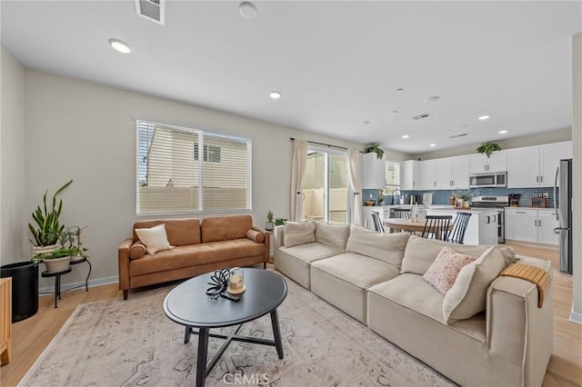 living room with light wood-style flooring, visible vents, baseboards, and recessed lighting