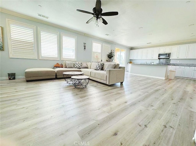 unfurnished living room with light wood-type flooring, baseboards, visible vents, and crown molding