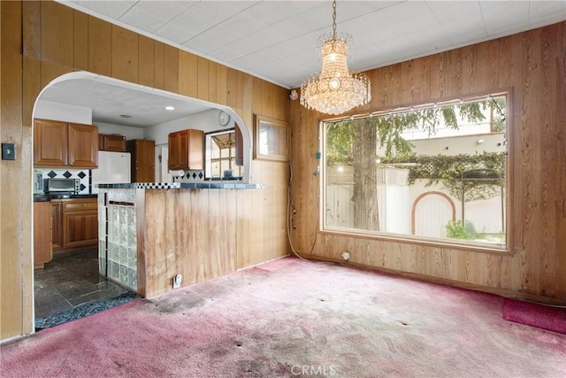 kitchen featuring carpet floors, arched walkways, wood walls, dark countertops, and brown cabinets