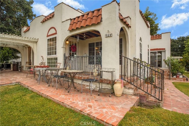 rear view of property with stucco siding, a patio, and a tile roof