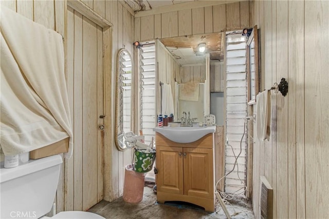 bathroom featuring wood walls, toilet, and vanity