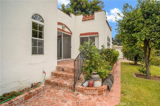 property entrance featuring stucco siding, a tiled roof, and a lawn