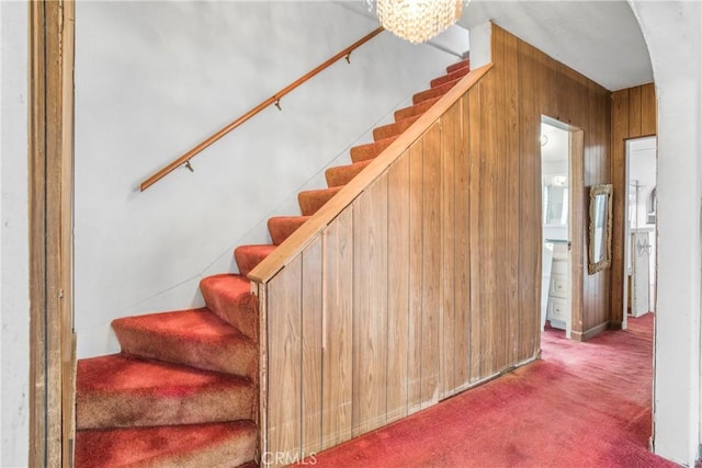 stairway featuring a notable chandelier, wooden walls, and carpet