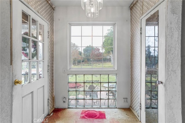 doorway with a chandelier, carpet flooring, and wallpapered walls