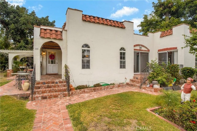 mediterranean / spanish home featuring a tile roof, a pergola, a front yard, and stucco siding