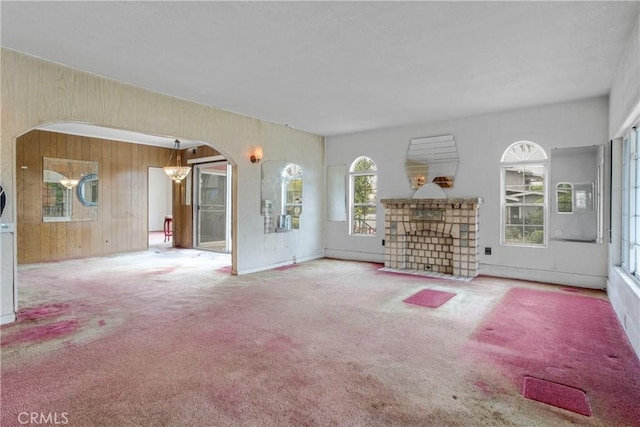 unfurnished living room with wooden walls, arched walkways, and carpet floors