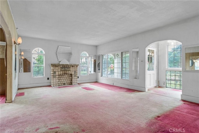 unfurnished living room featuring arched walkways, carpet, and a textured ceiling