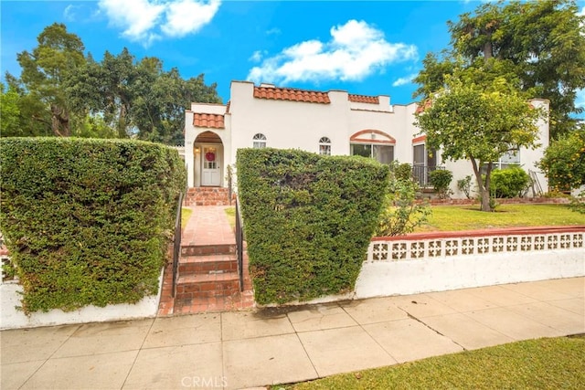 mediterranean / spanish house with a front yard, a tiled roof, and stucco siding