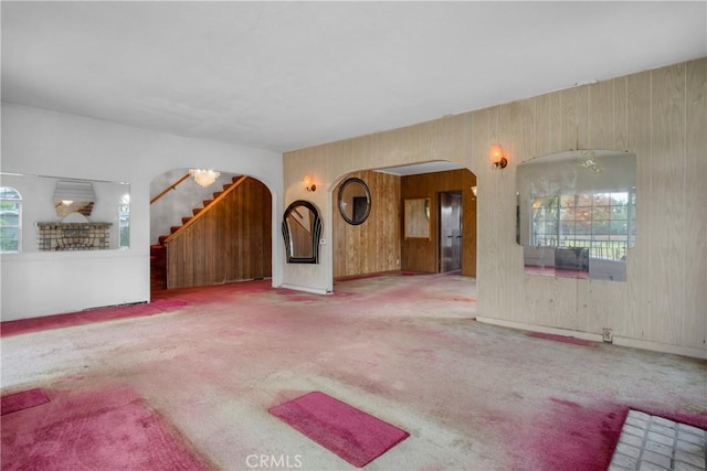 unfurnished living room with arched walkways, stairs, and carpet