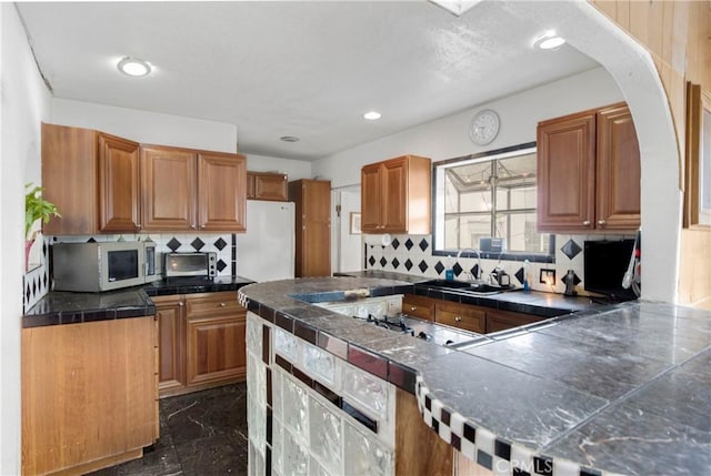 kitchen with tasteful backsplash, stainless steel microwave, freestanding refrigerator, marble finish floor, and a sink