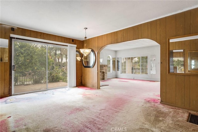 spare room with wooden walls, visible vents, carpet, a chandelier, and arched walkways