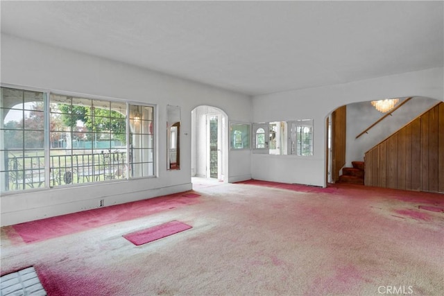 unfurnished living room with stairway, arched walkways, and carpet