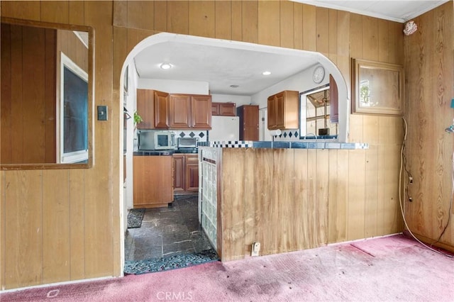 kitchen featuring dark carpet, freestanding refrigerator, wooden walls, a peninsula, and brown cabinetry