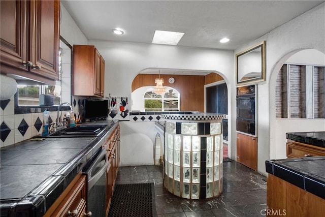 kitchen with tile countertops, a sink, decorative backsplash, dishwasher, and a chandelier