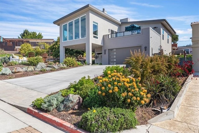 contemporary home with a garage, concrete driveway, a balcony, a carport, and stucco siding