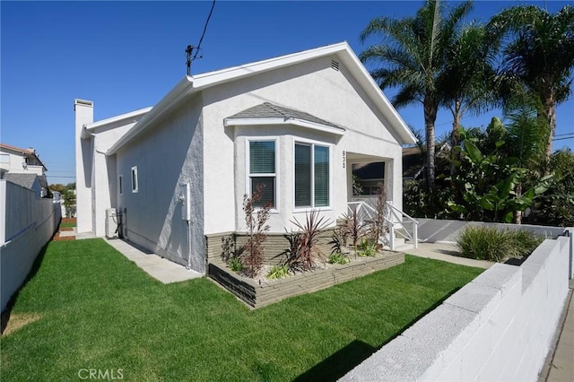 view of property exterior featuring a lawn, fence, and stucco siding